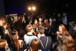 Wojciech Mecwaldowski pozuje do zdjęcia w trakcie Gali Sztuki Wyboru, w tle sala kinowa i duża liczba osób rozmawiających w grupach.
