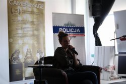 Magdalena Boczarska w fotelu w trakcie spotkania z młodzieżą, w tle banery Policja oraz Camerimage.